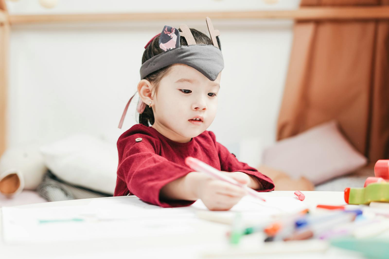 A young child wearing a headpiece enjoying drawing in an indoor playroom setting.